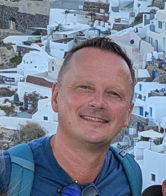 Sviat Kandakou in Greece, with white hillside buildings behind him